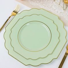 a green plate with gold trim sits on a white table cloth next to golden utensils