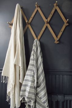 two towels are hanging on the wall next to a towel rack with hooks and wooden pegs