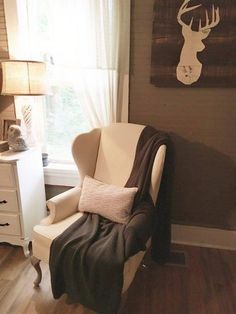 a chair with a blanket draped over it in front of a window and a deer head on the wall