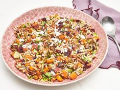 a pink bowl filled with food next to a spoon and napkin on top of a white table