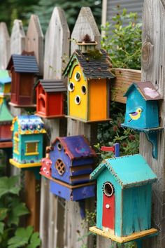 many colorful bird houses are hanging on the fence