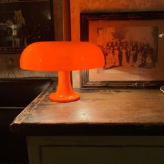 an orange table lamp sitting on top of a wooden counter next to a framed photograph