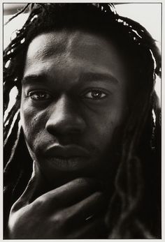 a black and white photo of a man with dreadlocks looking at the camera