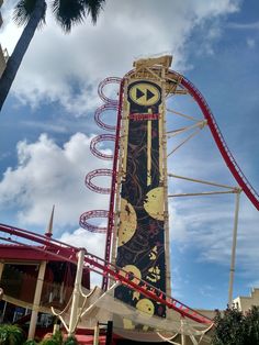 an amusement park with a roller coaster in the foreground and palm trees on the other side