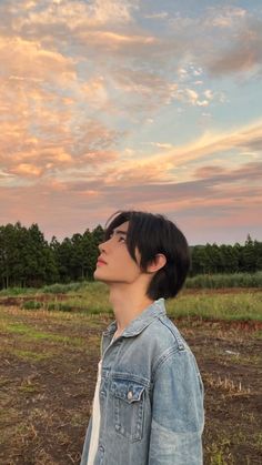 a person standing in the middle of a field looking up into the sky with trees in the background