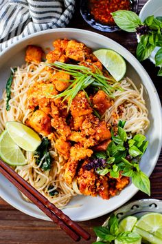 a white bowl filled with noodles and meat next to chopsticks on a wooden table