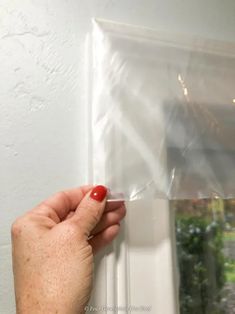 a hand holding a clear plastic sheet over a window sill with a red nail on it