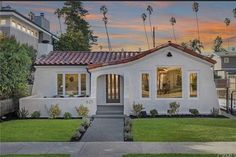 a white house with red tiled roof and palm trees in the background at sunset or dawn