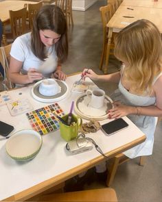 two women sitting at a table working on crafts