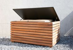 a wooden box with an open lid sitting on top of gravel next to a wall