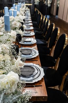 a long table is set with black and white plates, silverware, and flowers