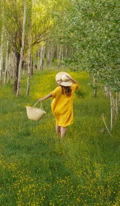 a woman in a yellow dress and straw hat walks through the woods with her basket