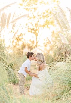 a couple kissing in tall grass during their engagement photo session at the beach with sun shining on them