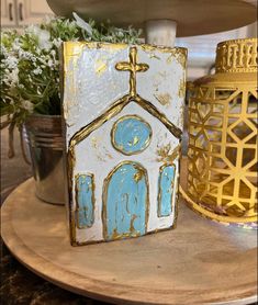 a small blue and white church painted on top of a wooden table next to potted plants