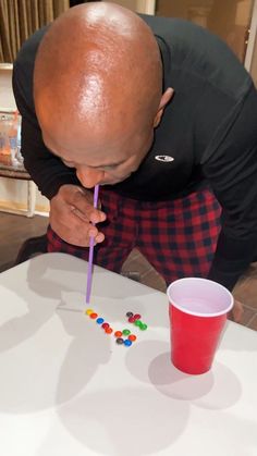 a man blowing out candy on top of a table next to a cup with a straw in it