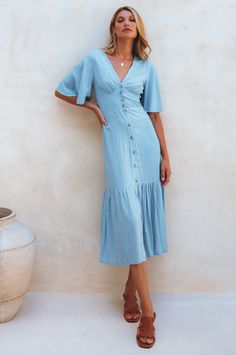 The simple yet charming Donna midi dress screams elegance and femininity. Handcrafted from soft breathable rayon into a button-down silhouette with a smock waist on the back and fitted detailing on the front it cascades into a tiered skirt and is adorned with tortoise buttons and butterfly sleeves. Style Donna with a pair of low-heel slides for the perfect coastal summer look. Content: 100% Rayon Hand wash warm Button-down silhouette Elasticated waist on the back Button-up closure Midi length Un Flowy Buttoned Dress For Brunch, Flowy Maxi Dress With Buttons For Brunch, Flowy Dresses With Buttons For Brunch, Summer Mid-length Dress With Button Closure, Chic Viscose Dress With Button Closure, Chic Flowy Dress With Buttons, Flowy Buttoned Midi Dress For Day Out, Flowy Viscose Midi Dress For Casual Wear, Knee-length Midi Dress With Buttons For Brunch