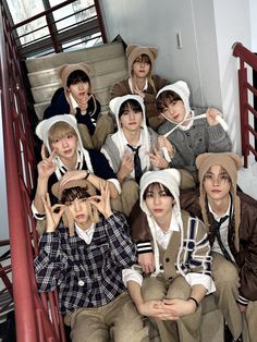 group of young men sitting on the steps wearing hats and scarves with their hands in the air