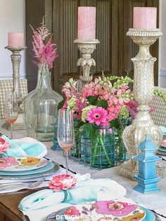 the table is set with pink and white flowers in glass vases, plates, and candles