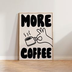 a poster with the words more coffee written in black and white, on a wooden floor