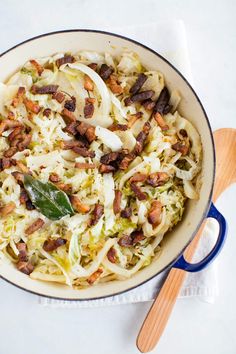 a bowl filled with cabbage and bacon on top of a white tablecloth next to a wooden spoon