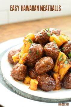 a white plate topped with meatballs covered in cheese and pineapple sauce on top of a wooden table