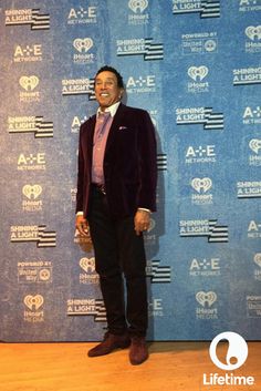 a man standing in front of a blue wall wearing a purple suit and pink tie