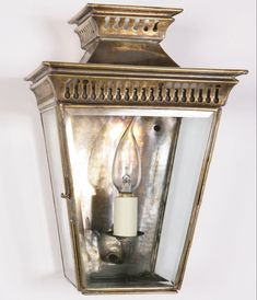 an old fashioned wall light with a candle on the front and side panels that have been painted gold