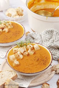 two bowls of soup with croutons and bread on the table next to it