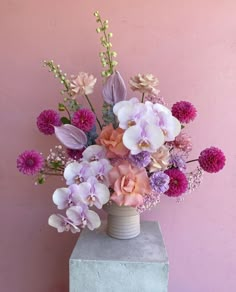 a vase filled with pink and purple flowers on top of a cement block in front of a pink wall