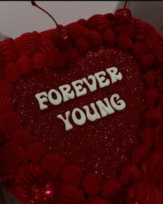 a red heart shaped cake with the words forever young on it's side and white lettering