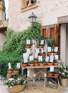 there are many potted plants on the table in front of the house with cards attached to them