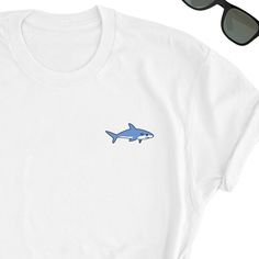 We have express delivery for our shirts! 📦⚡.  From cart to door in just 2-3 days, only for 3.5 USD extra.  You can find the express delivery option in the cart. Shark Shirt, Cute Shark Tee Shirt, Shark Tee Top, Cute Shark T-Shirt,  Shark Icon Gift Shirt, Shark Lover Friends UNISEX Shirt Gift, Shark Friends will love it! This t-shirt feels soft and lightweight, with the right amount of stretch. It's comfortable and flattering for both men and women.  * 100% cotton (heather colors contain polyester) * Fabric weight: 5 oz  * Shoulder-to-shoulder taping * Side-seamed Time for Delivery: * Processing & production time is 1-6 business days (usually 2-3 days). * U.S. Shipping time: 3-5 business days.  * International shipping time: 4-15 days. - Please note European customers: Some orders going to White Basic T-shirt With Funny Print, White Crew Neck Shirt With Funny Print, Beachy Clothes, Shark Tee, Shark Lover, Shark Shirt, Shark T Shirt, Cute Shark, Lovers And Friends