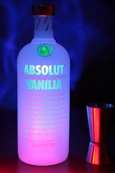 an illuminated bottle sitting on top of a table next to a shot glass and shaker