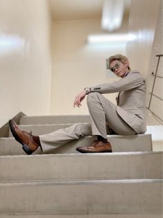 a man sitting on some stairs with his legs crossed and wearing sunglasses, looking at the camera