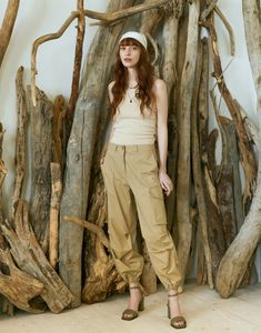 a woman is standing in front of some driftwood branches and wearing a hat with her hands on her hips