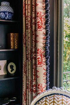 a room with a chair, bookshelf and window that has curtains on it