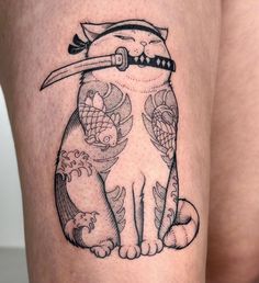 a woman's thigh with a cat tattoo on it and a knife sticking out of her mouth