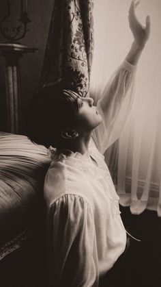 a woman laying on top of a bed next to a window with curtains behind her