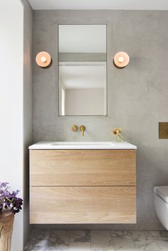 a white toilet sitting next to a bathroom sink under a mirror and two lights on the wall