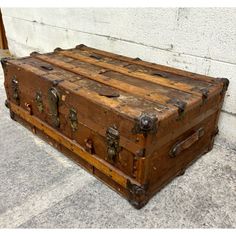 an old wooden trunk is sitting on the concrete floor in front of a white wall