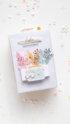 a card with flowers and a camera on it, next to confetti sprinkles