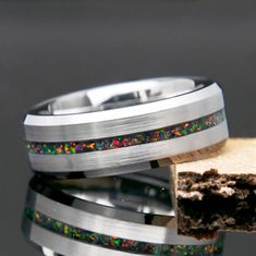 two wedding bands with multicolored opal inlays on each band, one is made from stainless steel and the other is silver