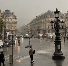 people walking in the rain with umbrellas on a city street near buildings and lamps