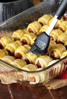 a person using a spatula to dip hotdogs into a casserole dish