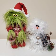 two stuffed animals dressed in christmas clothes and hats, one is white the other has green hair