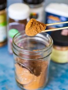 a spoon with some food in it on top of a glass jar filled with spices