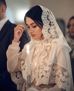 a woman wearing a veil and holding a lit candle in her hand while standing next to a man