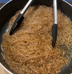 noodles being cooked in a pan with tongs