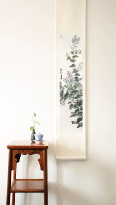 a small wooden table sitting next to a wall with a painting hanging on it's side