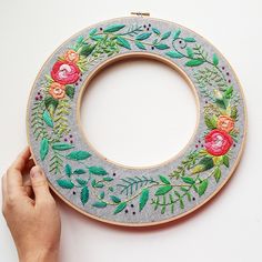 a hand is holding a embroidery hoop with flowers and leaves on it, while another hand holds the hoop